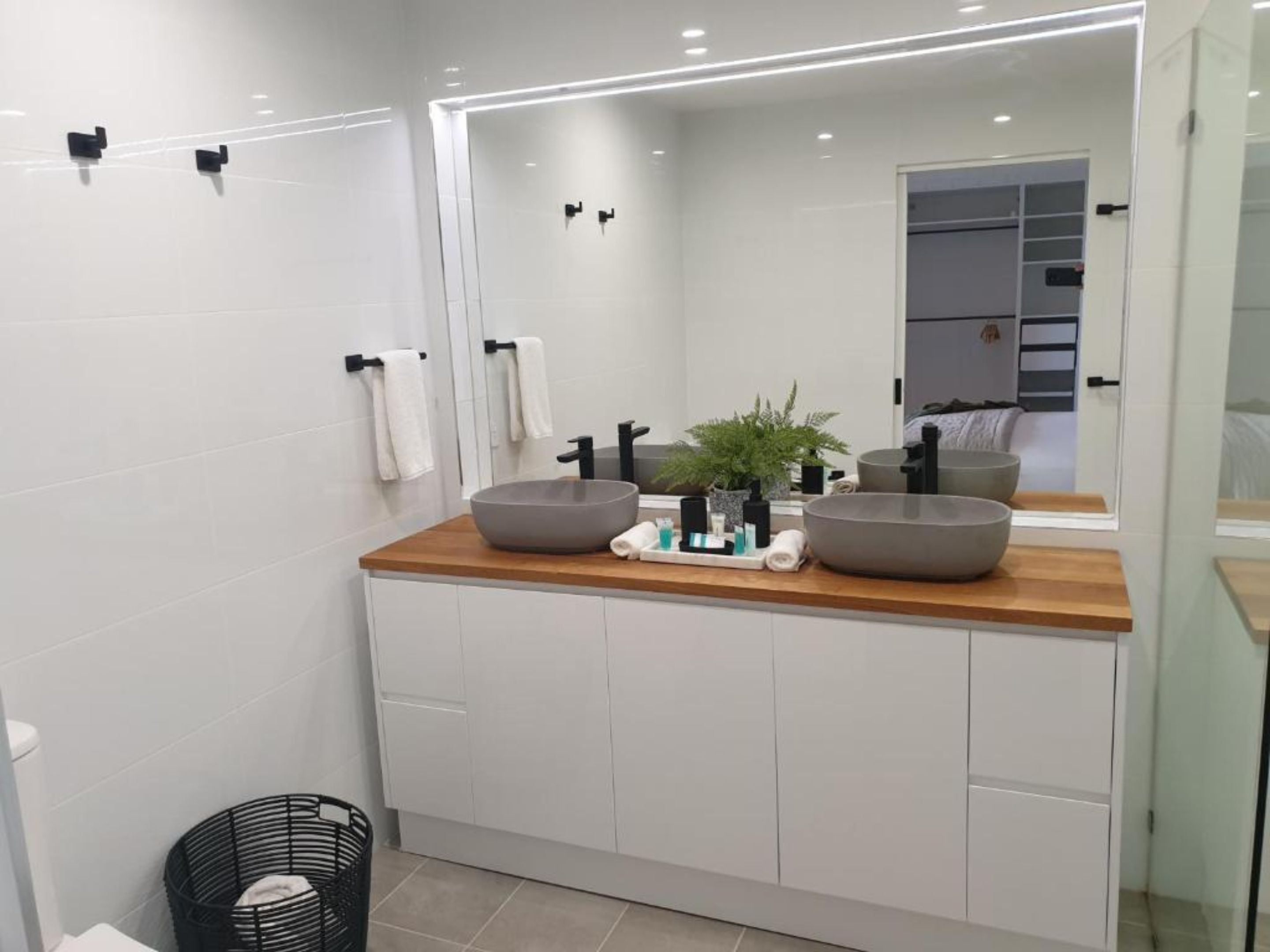 A modern bathroom with a wooden vanity, two large sinks, a mirror, and a potted plant.