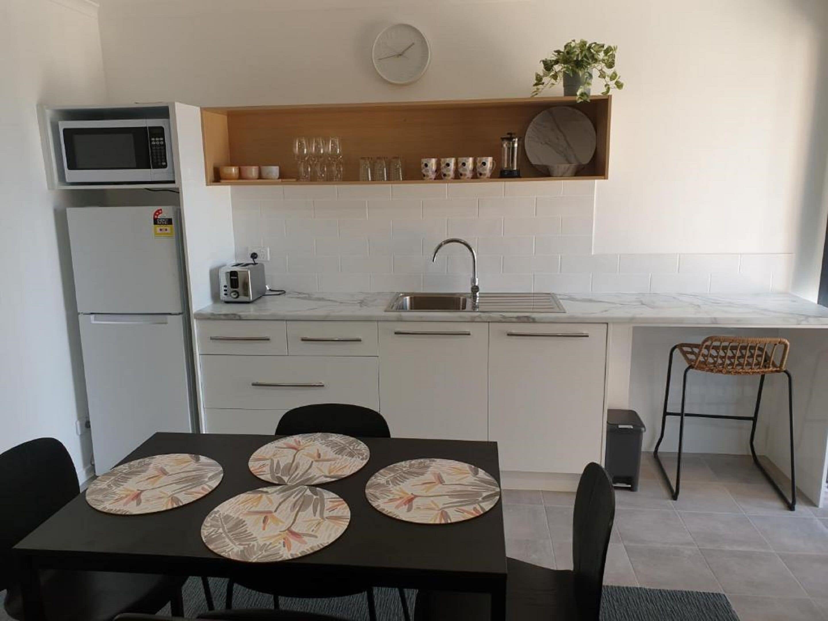 Cocina compacta equipada con microondas, tostadora, lavamanos y un pequeño comedor con mesa y sillas.
