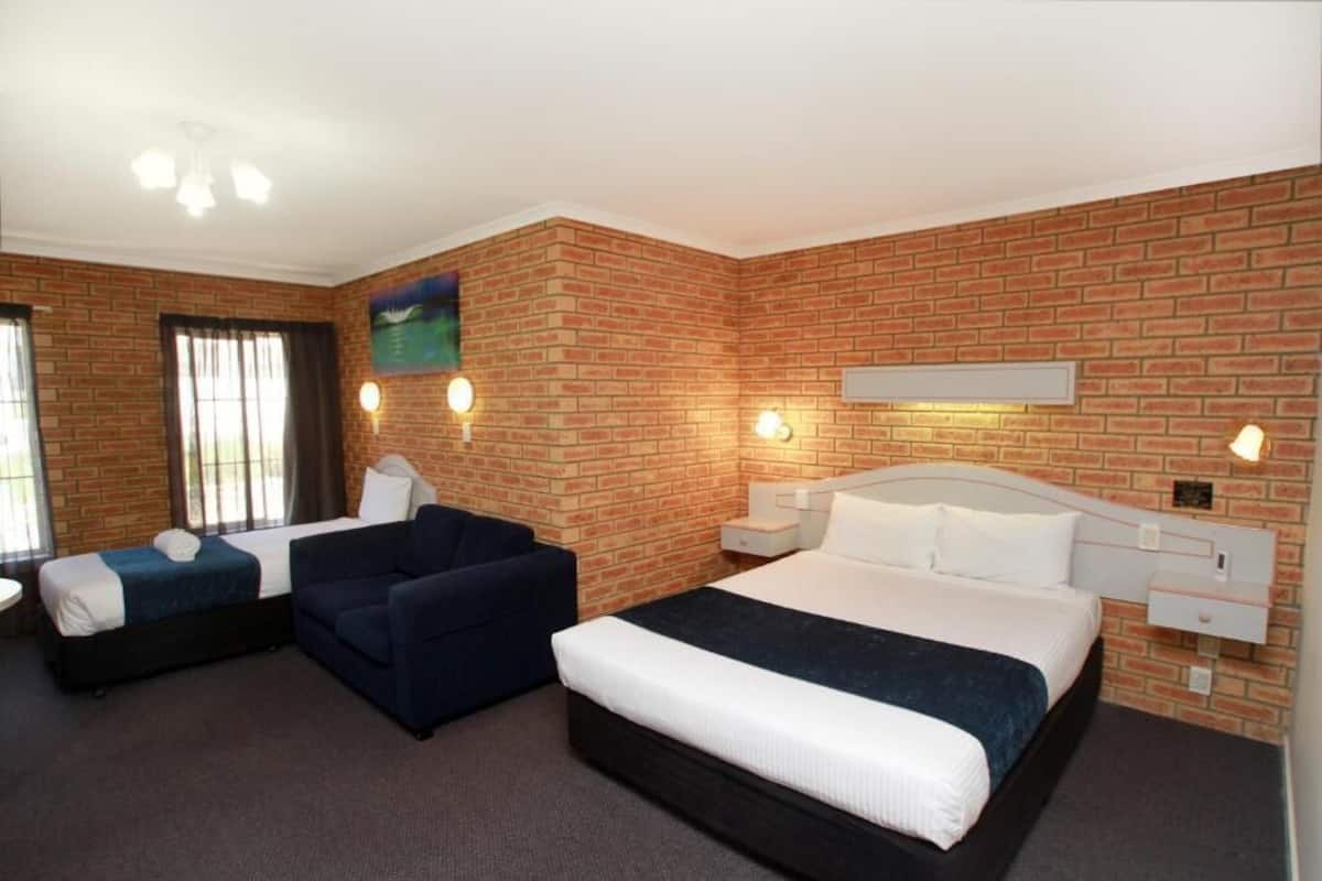 A hotel room with a brick wall, two beds, a sofa, and a ceiling fan.