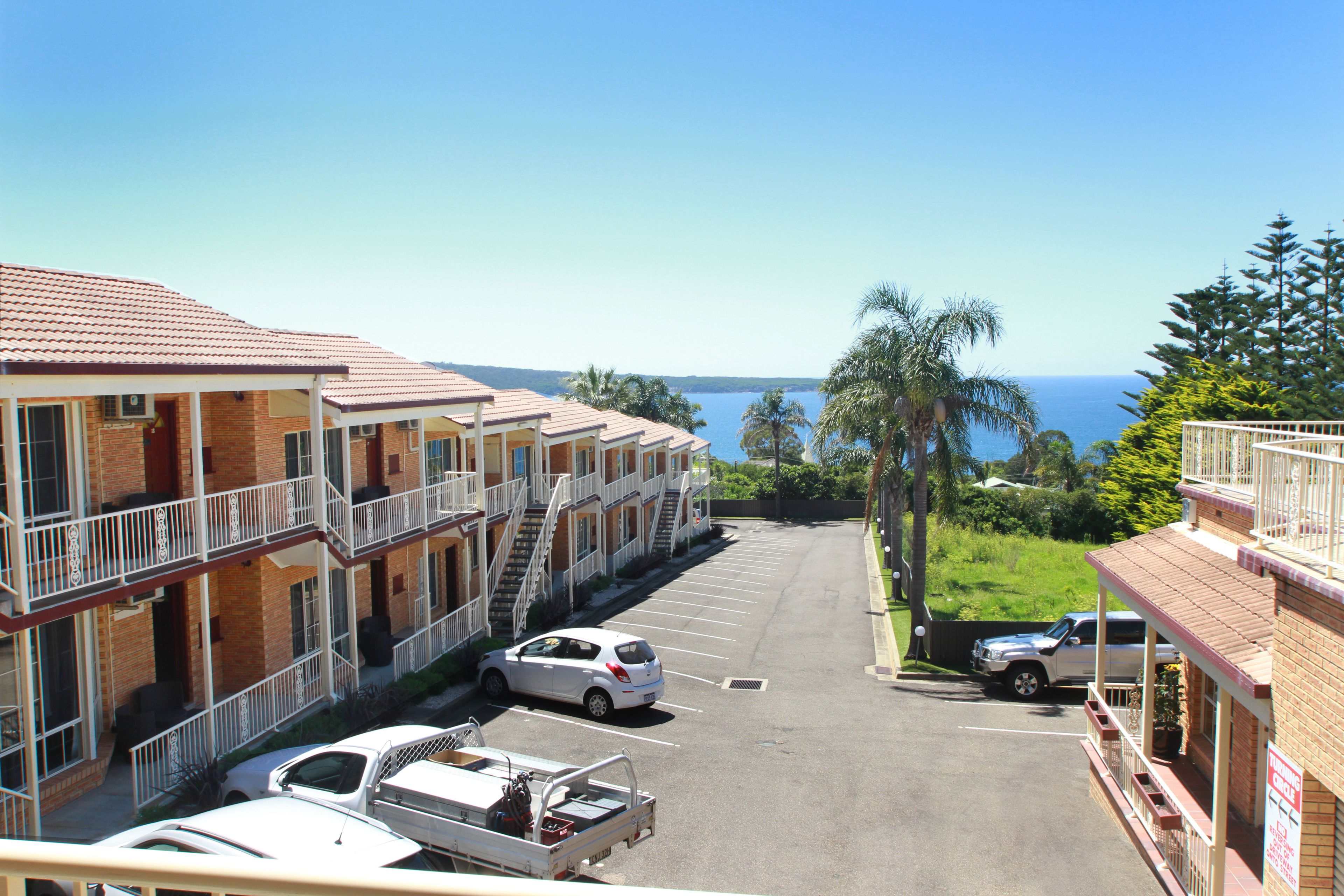 A row of motel buildings with a parking lot, a small truck, and a car parked in front.