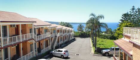 A row of motel buildings with a parking lot, a small truck, and a car parked in front.