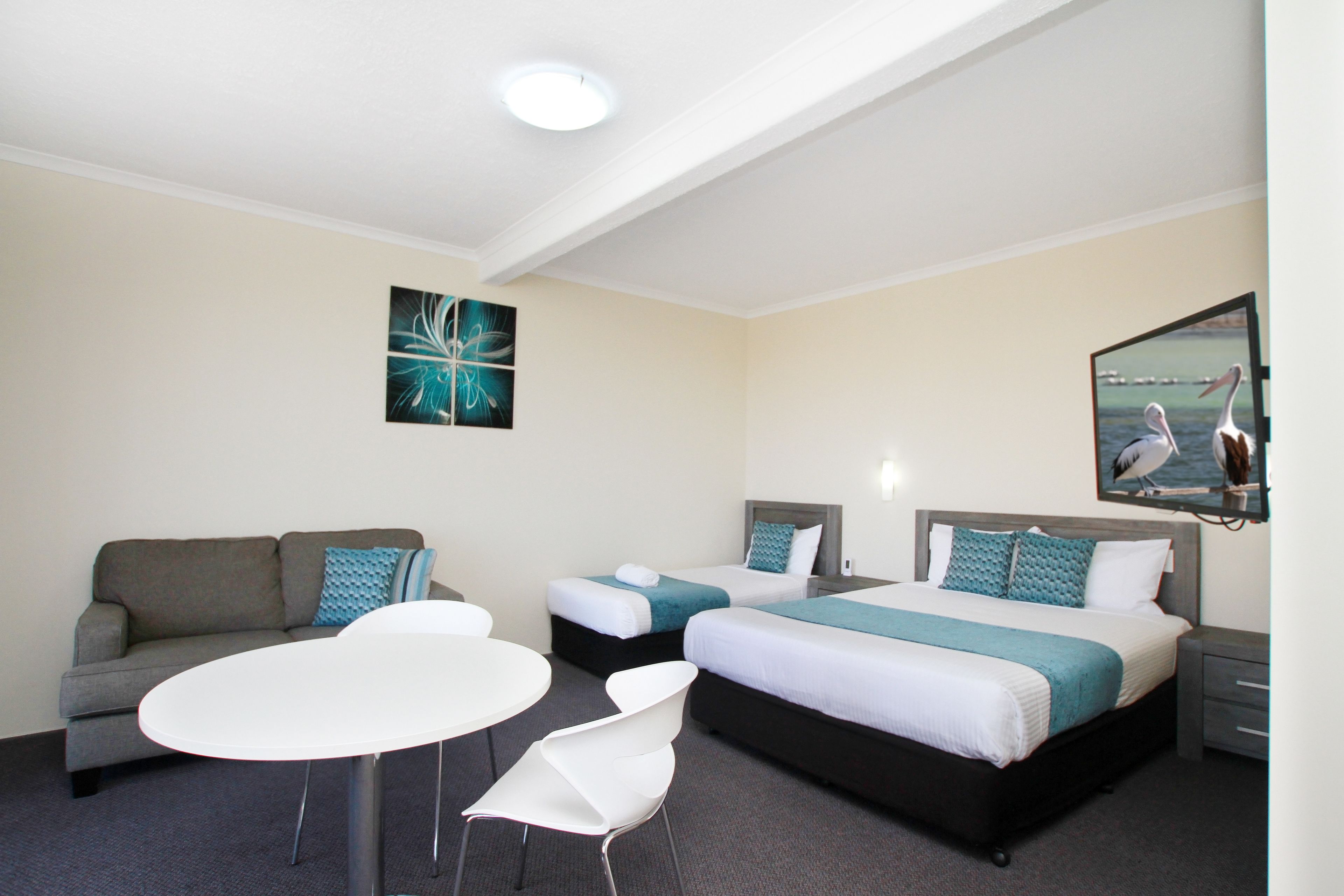 A hotel room with a sofa, two single beds, a small table, and a chair.