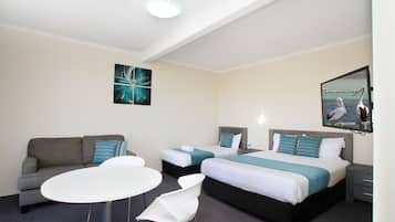 A hotel room with a sofa, two single beds, a small table, and a chair.