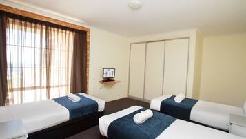 Two single beds with white linens and dark bedspreads, a large window, and a small shelf with a framed picture.