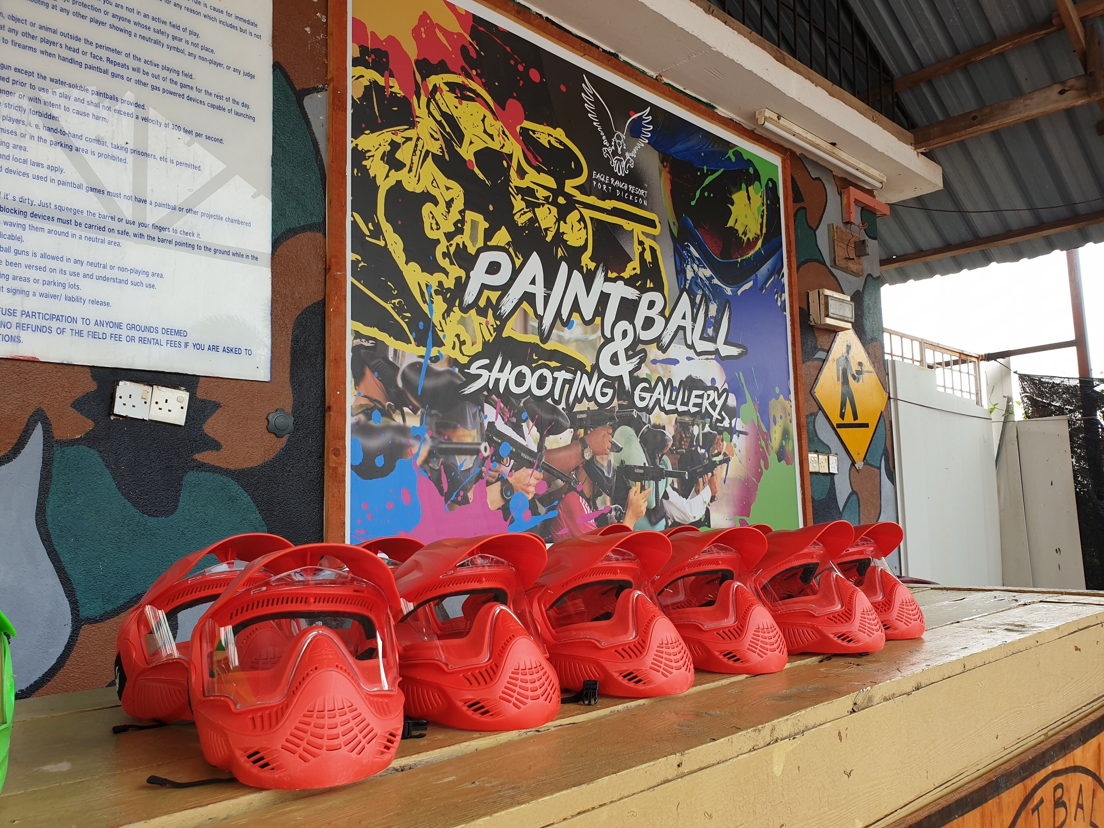 A wall with a colorful mural advertising a paintball and shooting gallery.
