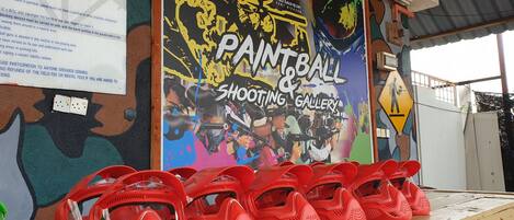 A wall with a colorful mural advertising a paintball and shooting gallery.