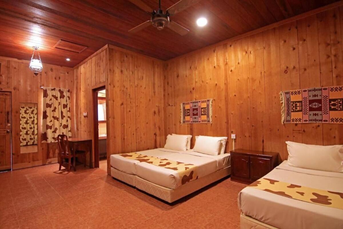 A wooden room with two beds, a ceiling fan, and a dining table.