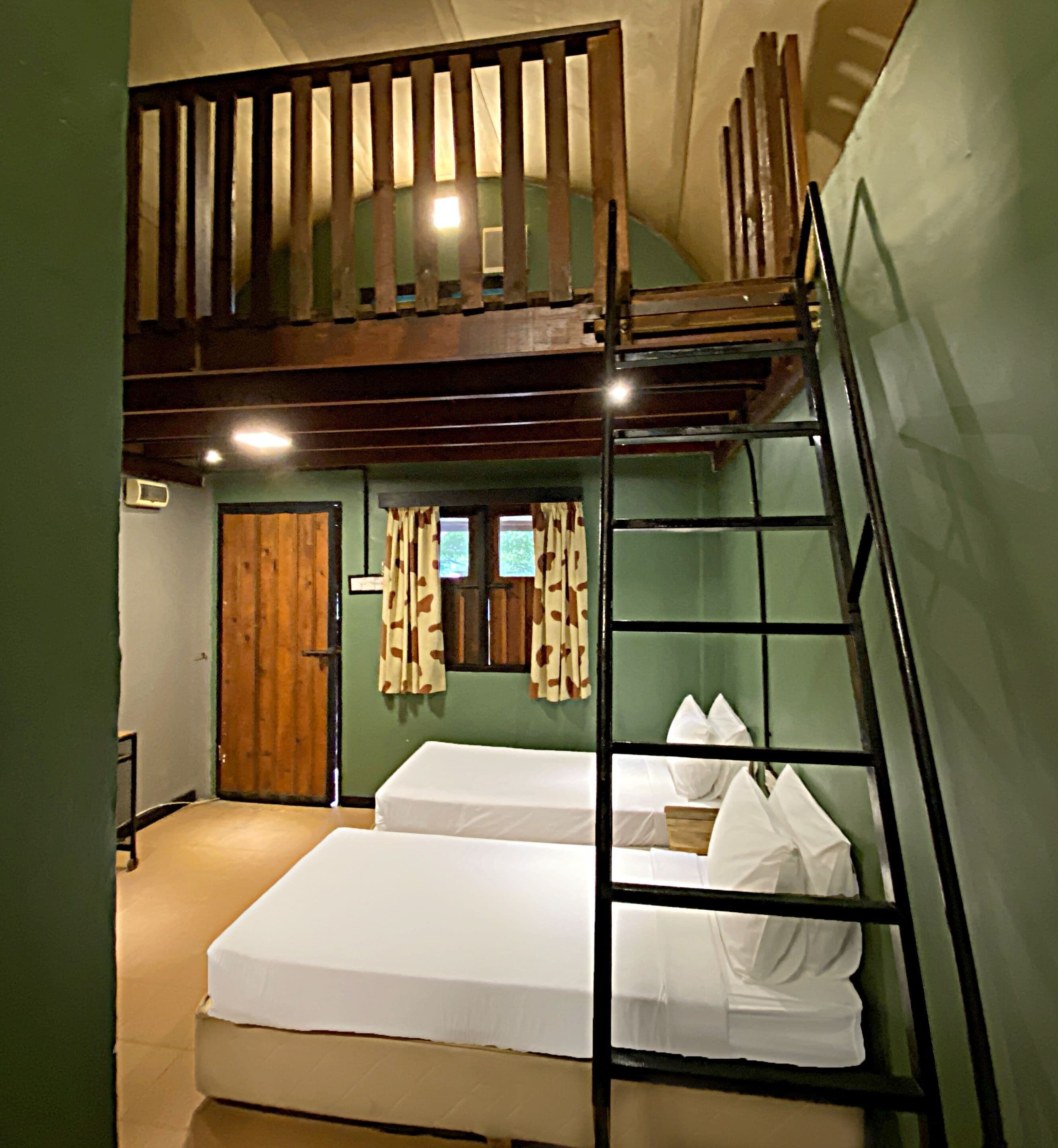 A dormitory room with bunk beds, a wooden ladder, a door, and a window with curtains.