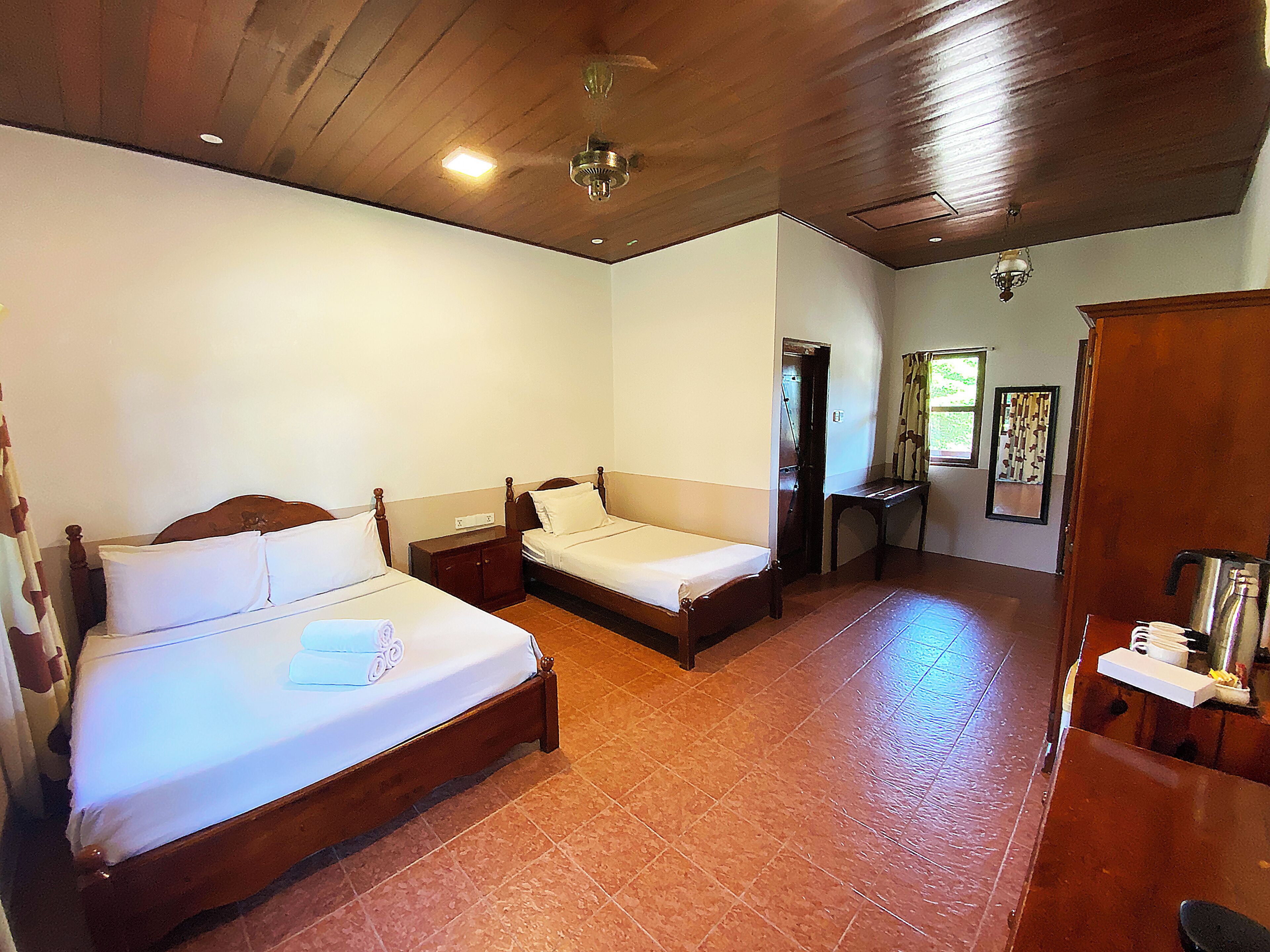 A room with two wooden beds, a wooden wardrobe, and a small table with a kettle.
