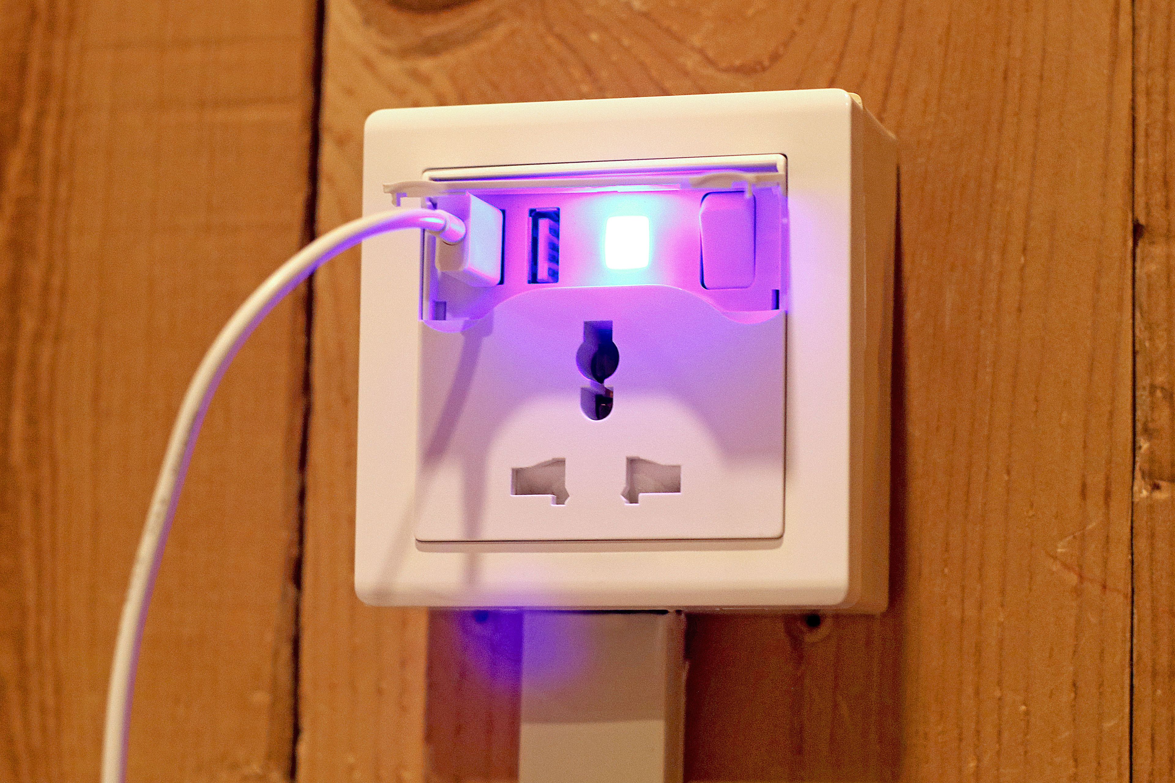 A white electrical outlet with a USB port and a power cord plugged in, mounted on a wooden surface.
