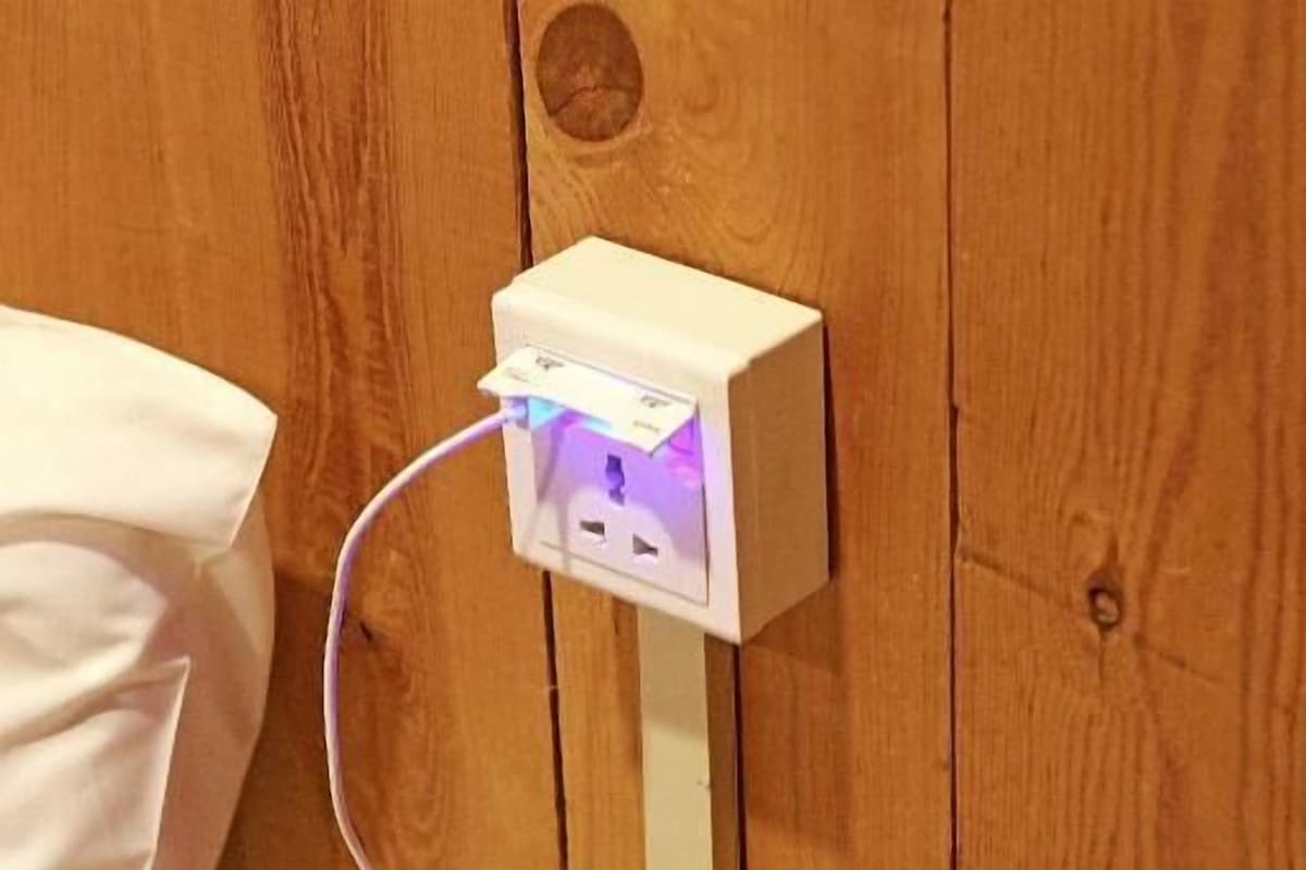 A smartphone on a wooden nightstand with a white power strip and a white pillow.