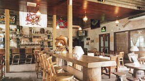 A rustic bar with wooden furniture, a long counter, and hanging flags. - Eagle Ranch Resort (Port Dickson)