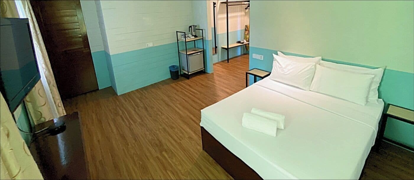 A hotel room with a bed, a small table, a shelf with toiletries, and a television.