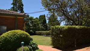 A brick pathway leading to a building with a tiled roof, surrounded by well-maintained hedges and trees. - Katoomba Townhouses (Katoomba)