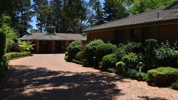 A brick building with a tiled roof, surrounded by well-maintained hedges and trees. - Katoomba Townhouses (Katoomba)