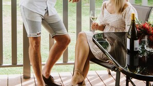 A man and a woman sitting at an outdoor table with a bottle of wine and a glass of wine.