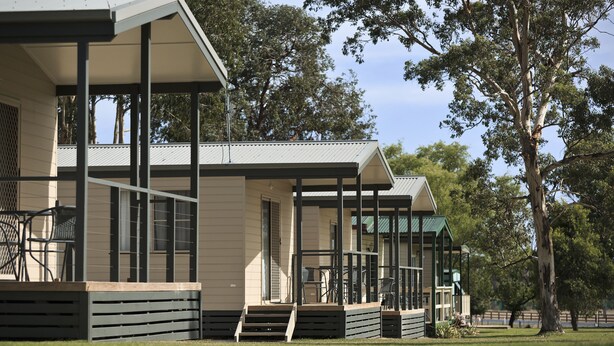 A modern building with a covered outdoor area, featuring a patio with chairs and a small table.