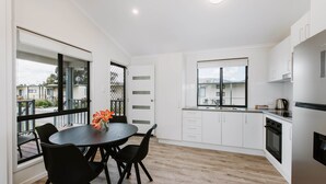 A modern kitchen with white cabinets, a dining area with a black table and chairs, and large windows offering views of the surrounding area.