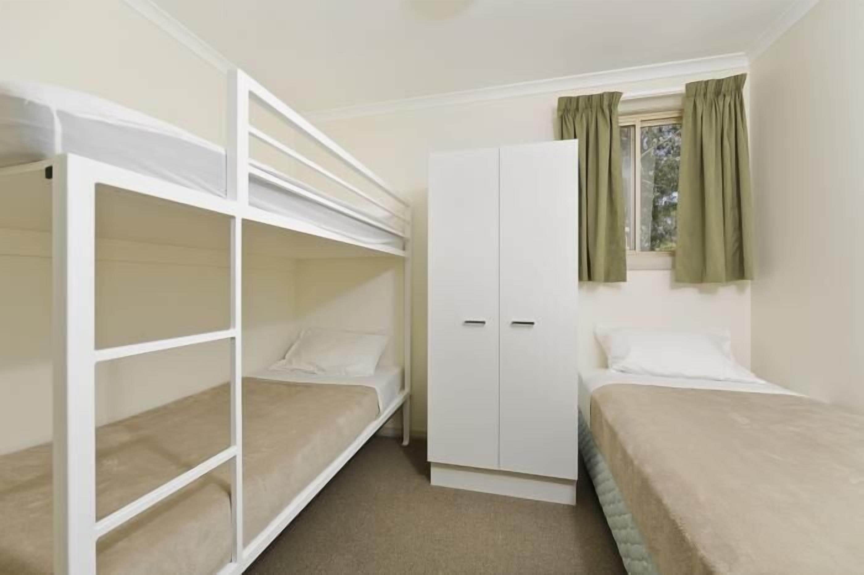 Um quarto de dormitório com beliches, guarda-roupa e janela com cortinas.