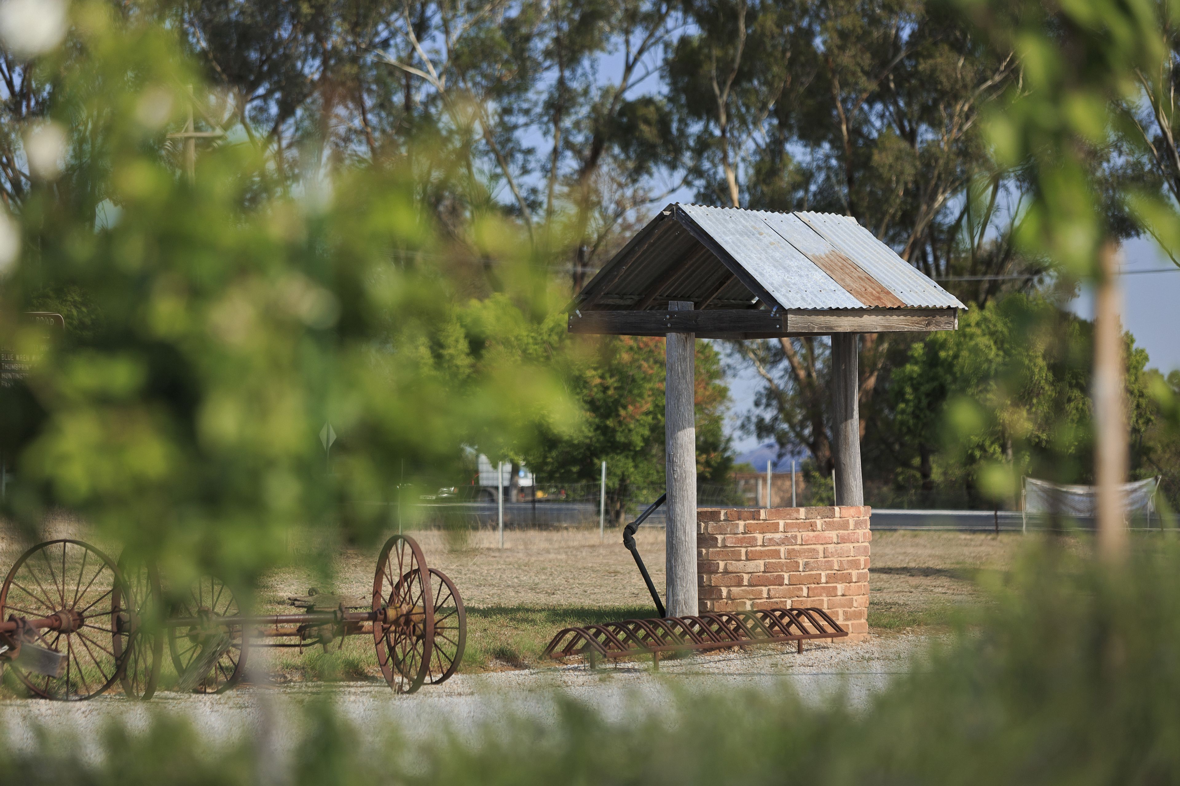 A rustic wooden structure with a metal roof, surrounded by a grassy area and a large, rusted wheel.