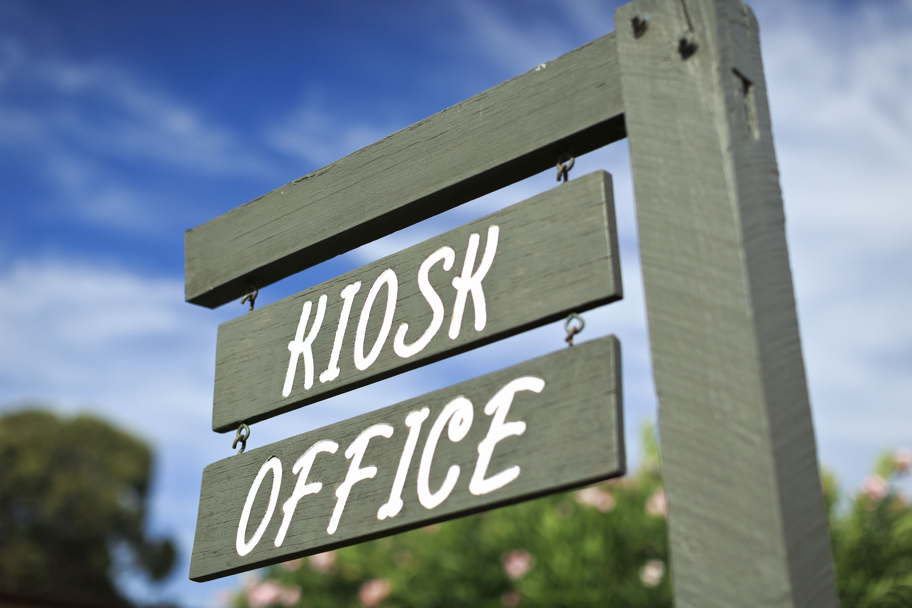 Un panneau en bois sur lequel on peut lire les mots « KIOSK OFFICE », le tout sur fond de ciel bleu.