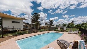 A swimming pool with lounge chairs and a covered area, surrounded by a fence and greenery.