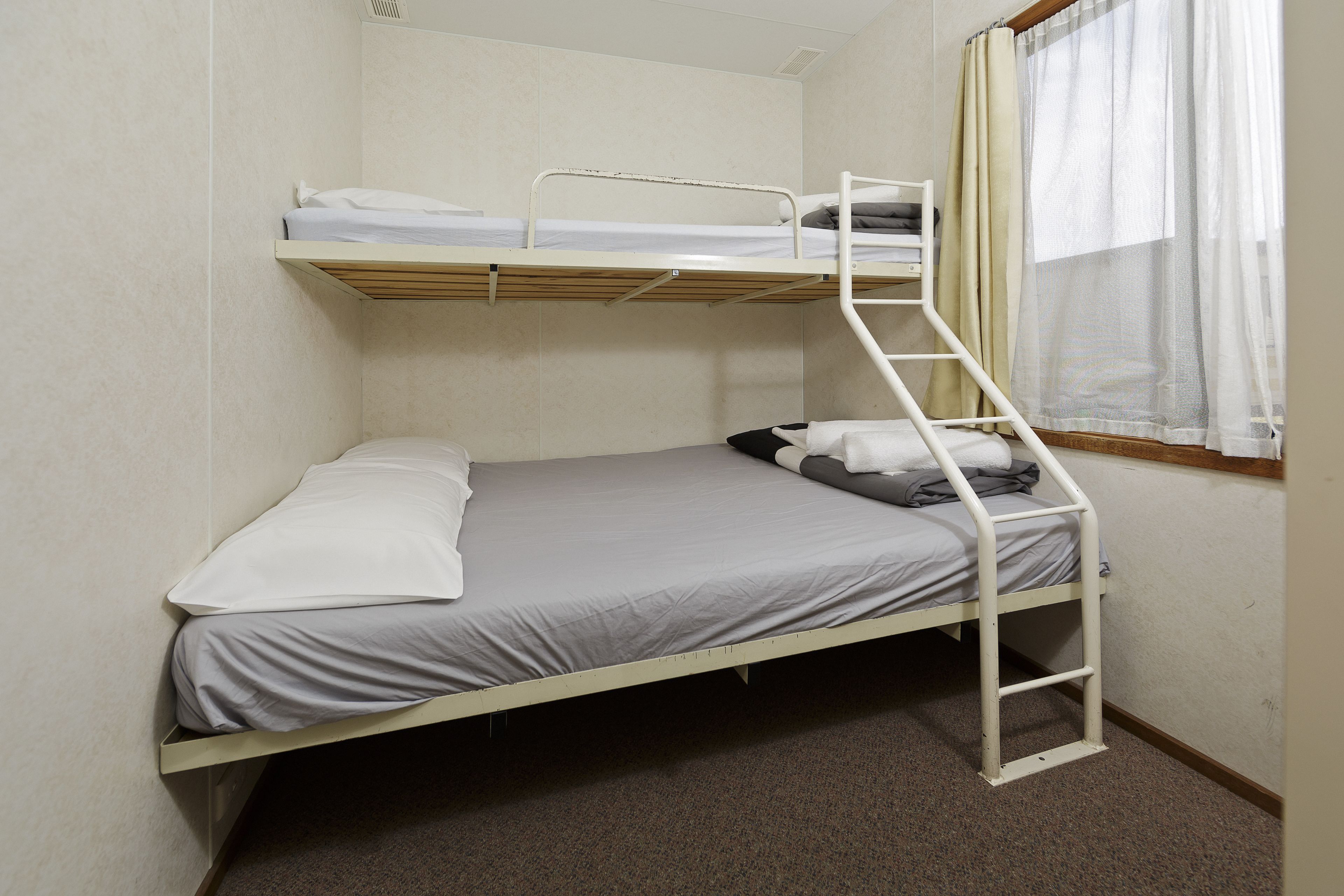 A bunk bed with a ladder, a window with curtains, and a plain wall.