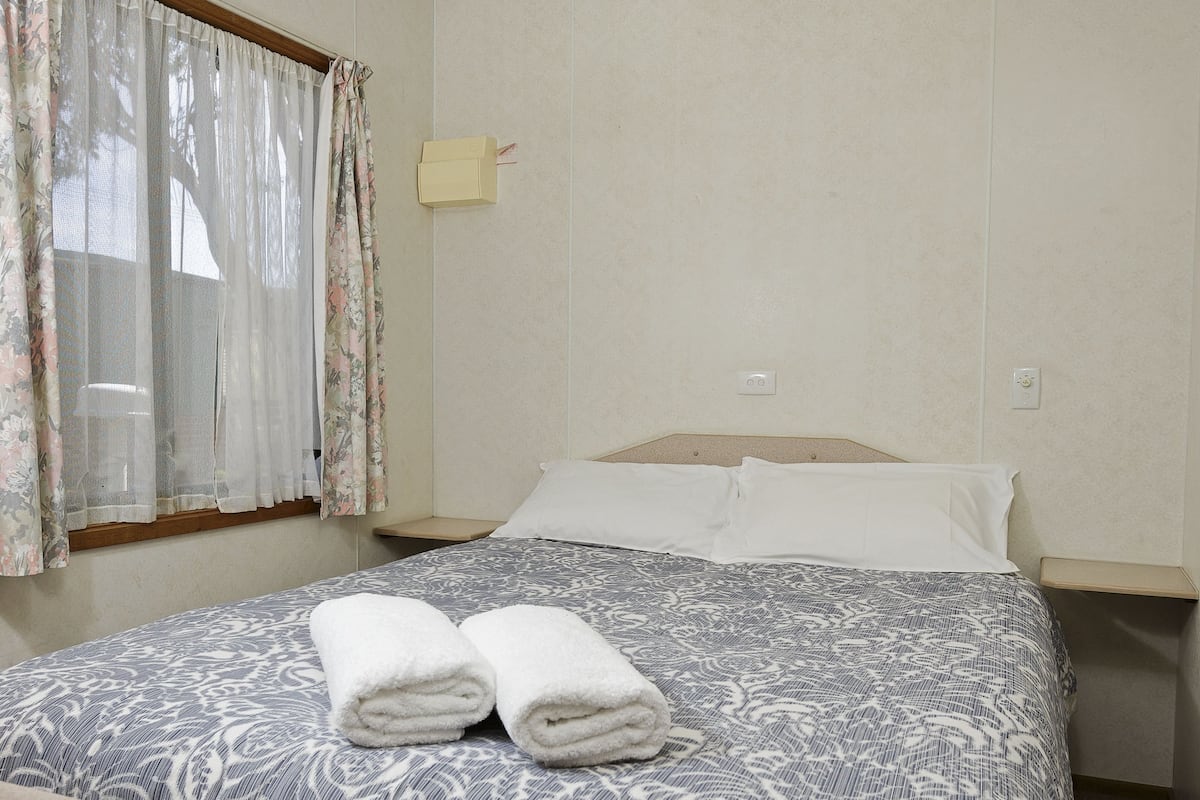 A neatly made bed with a patterned bedspread and two rolled towels on it.