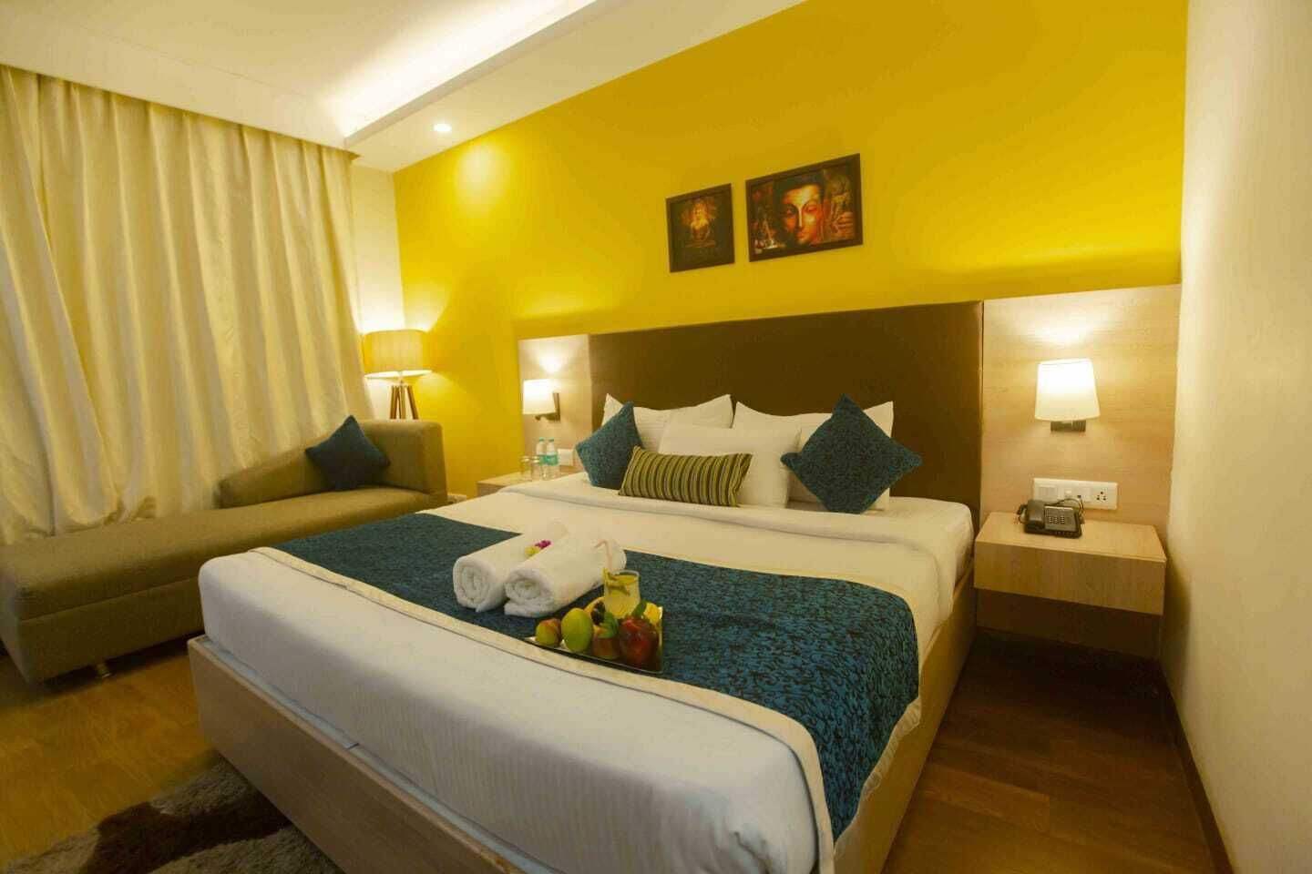 A hotel room with a large bed, a sofa, two bedside lamps, and a nightstand with a phone.