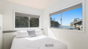 A bedroom with a bed, two windows, and a view of a beach and trees.