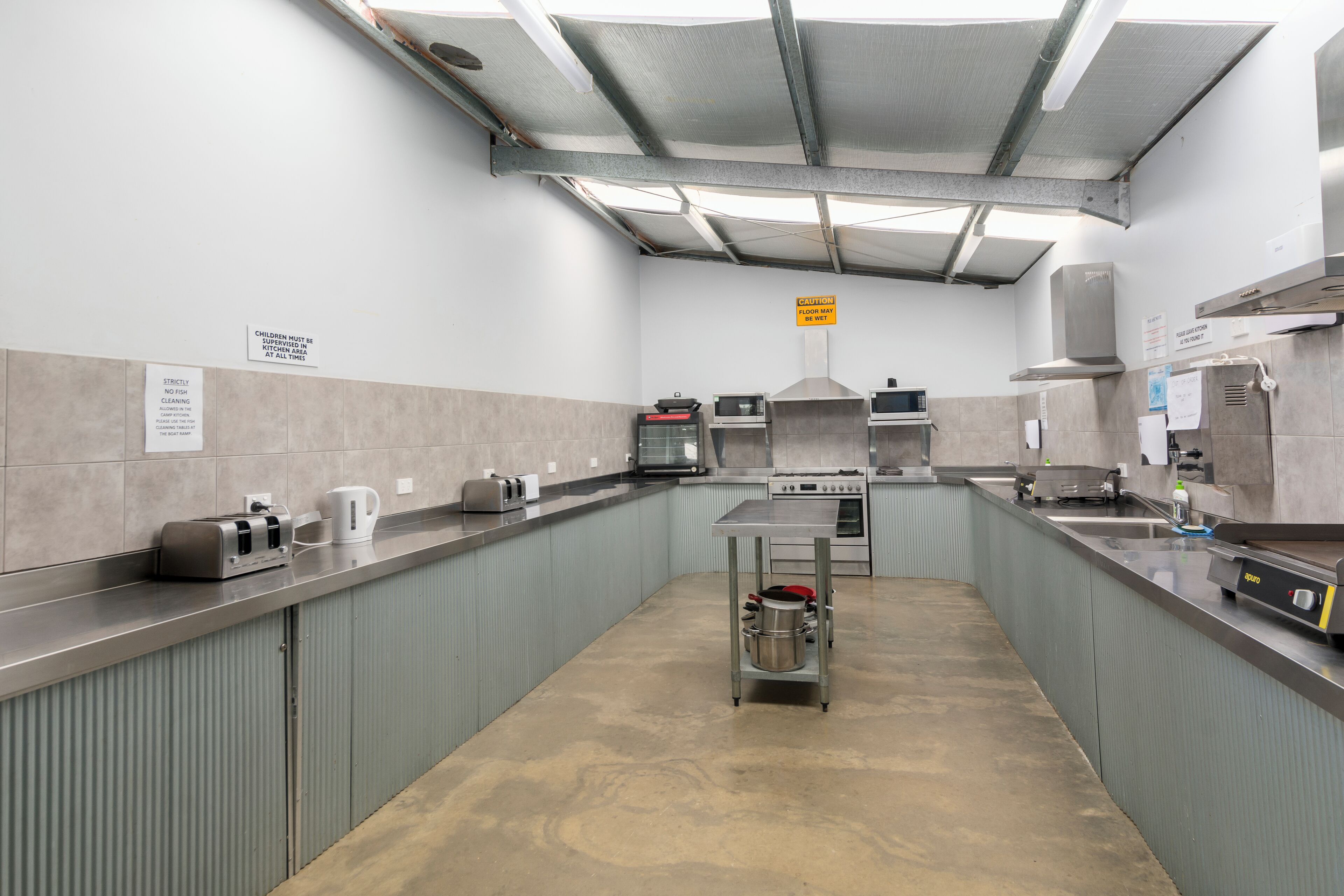 A kitchen with stainless steel appliances, a microwave, and a stove. There are signs indicating kitchen rules and a caution about the floor.