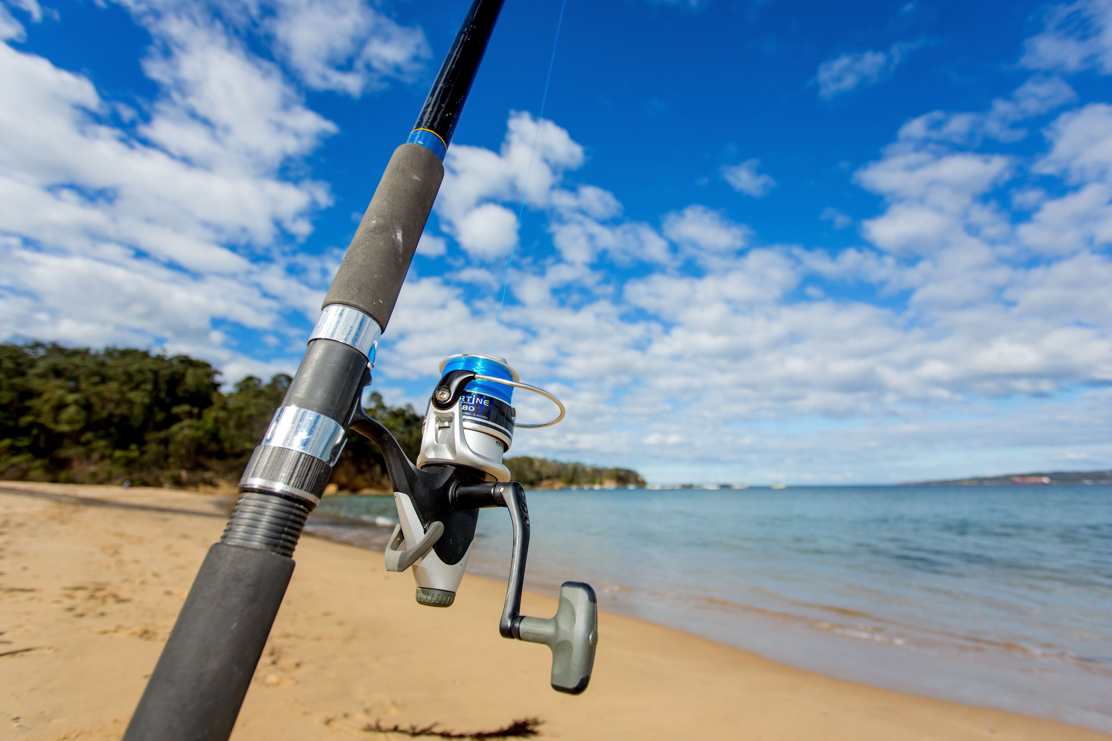 A fishing rod with a reel on a sandy beach with a clear sky.