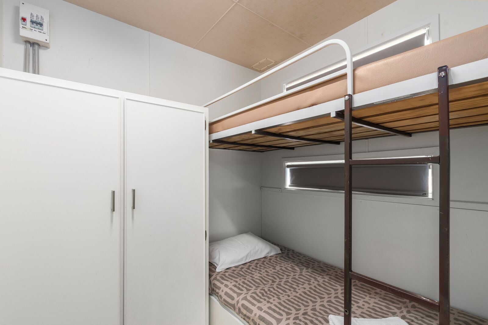 Un lit superposé avec un matelas à motifs, une armoire blanche et un luminaire fixé au plafond.