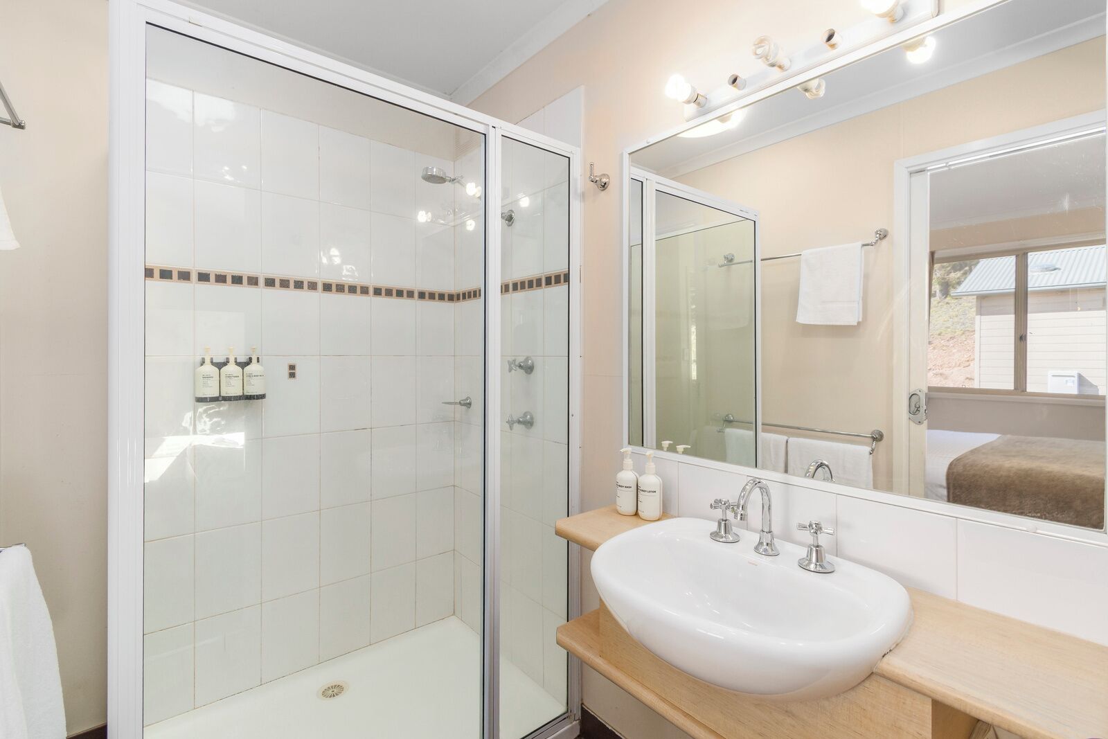 A bathroom with a glass-enclosed shower, a white sink with a wooden countertop, and a large mirror above the sink.