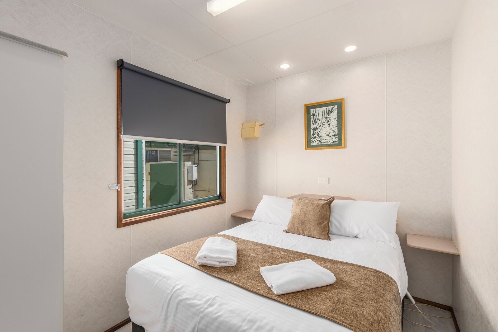 A hotel room with a bed, a window with a view, a framed artwork on the wall, and a bedside table.