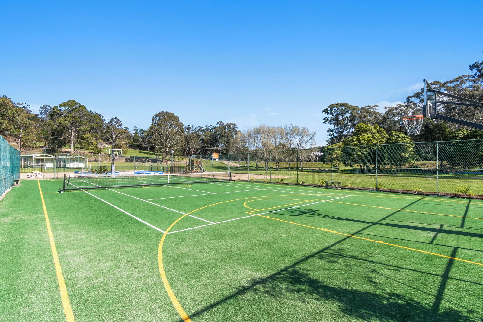 An outdoor basketball court with a net, surrounded by a fence and trees.