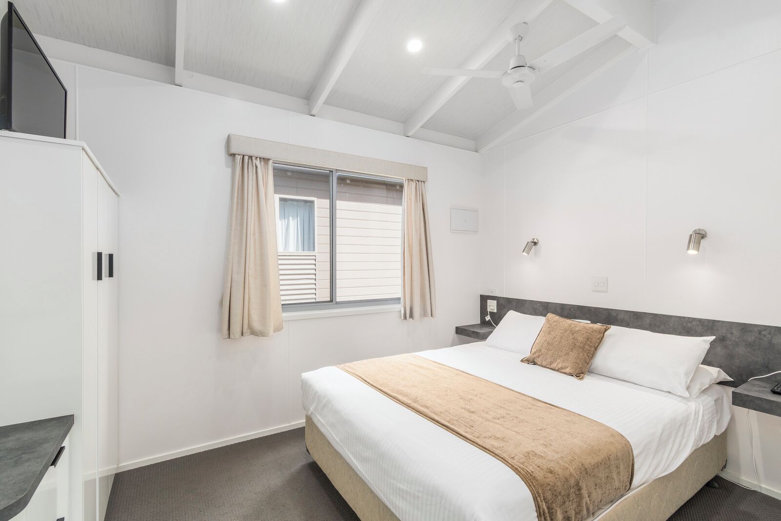 Une chambre à coucher avec un lit, une fenêtre avec des rideaux, une table de chevet et un ventilateur de plafond.