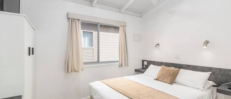 Une chambre à coucher avec un lit, une fenêtre avec des rideaux, une table de chevet et un ventilateur de plafond.