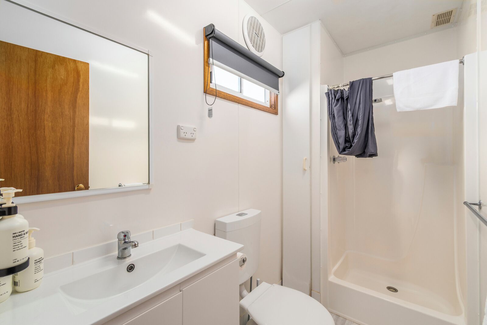 A bathroom with a white sink, mirror, and toilet. There is a shower with a curtain and a towel hanging on the wall.