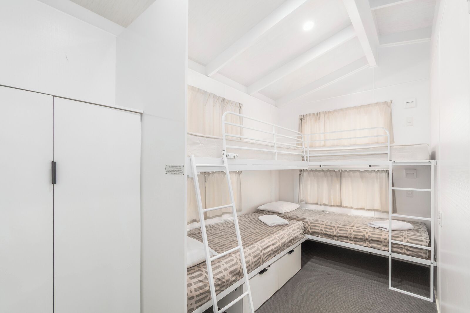 Quarto com beliche, guarda-roupa e janela com cortinas.