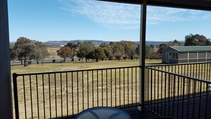 Ein Balkon mit Blick auf ein grasbewachsenes Feld, Bäume und ein entferntes Gebäude.