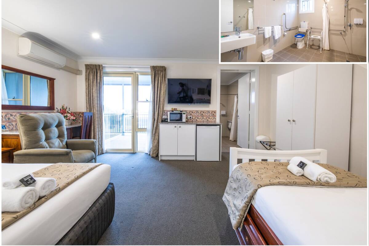 Habitación de hotel con cama, escritorio, televisor, baño con ducha y balcón.