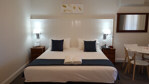 Ein Hotelzimmer mit einem großen Bett, zwei Nachttischen, einem Schreibtisch und einem Sessel.