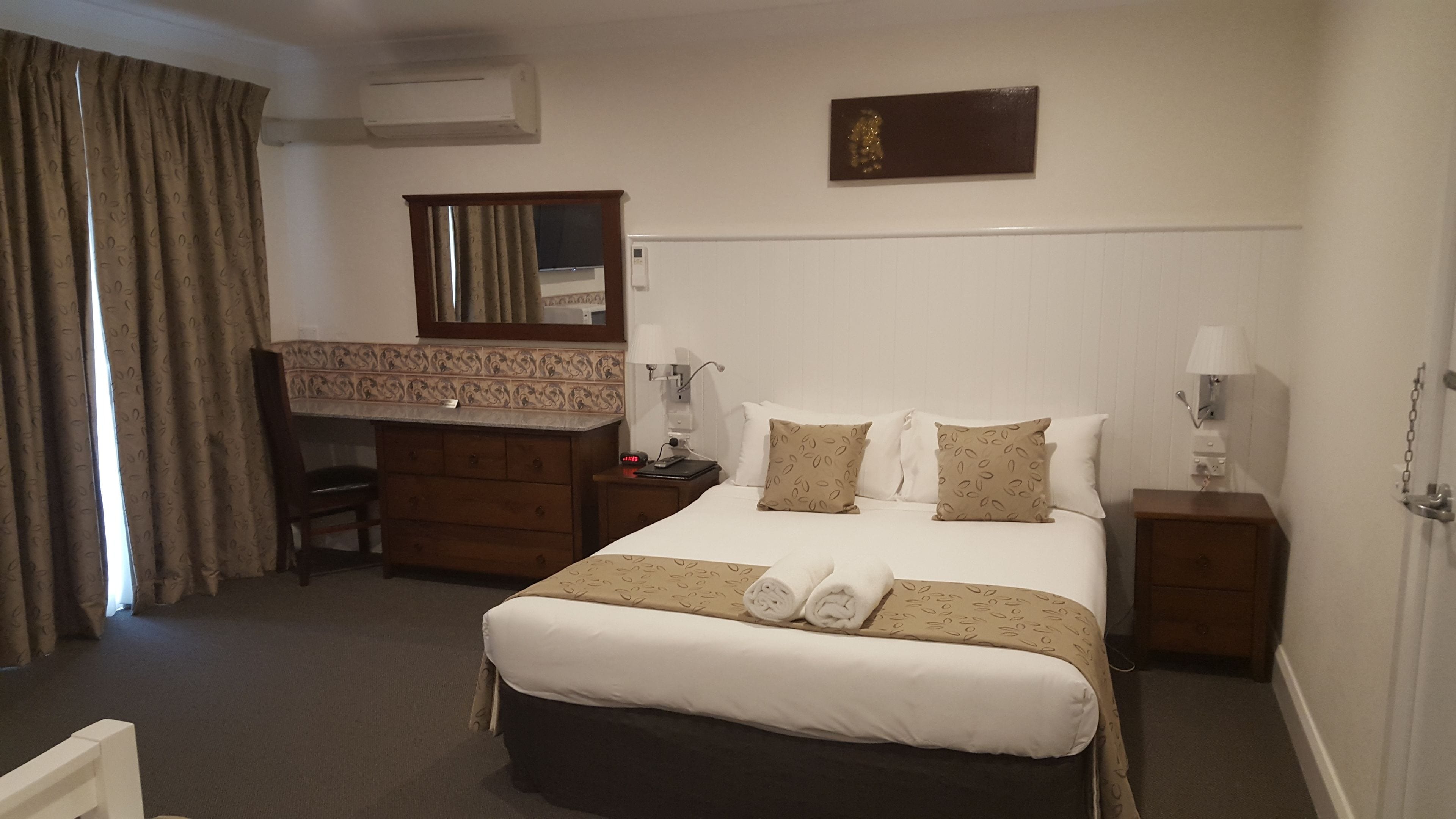 A hotel room with a bed, a desk, a chair, a dresser, and a mirror.