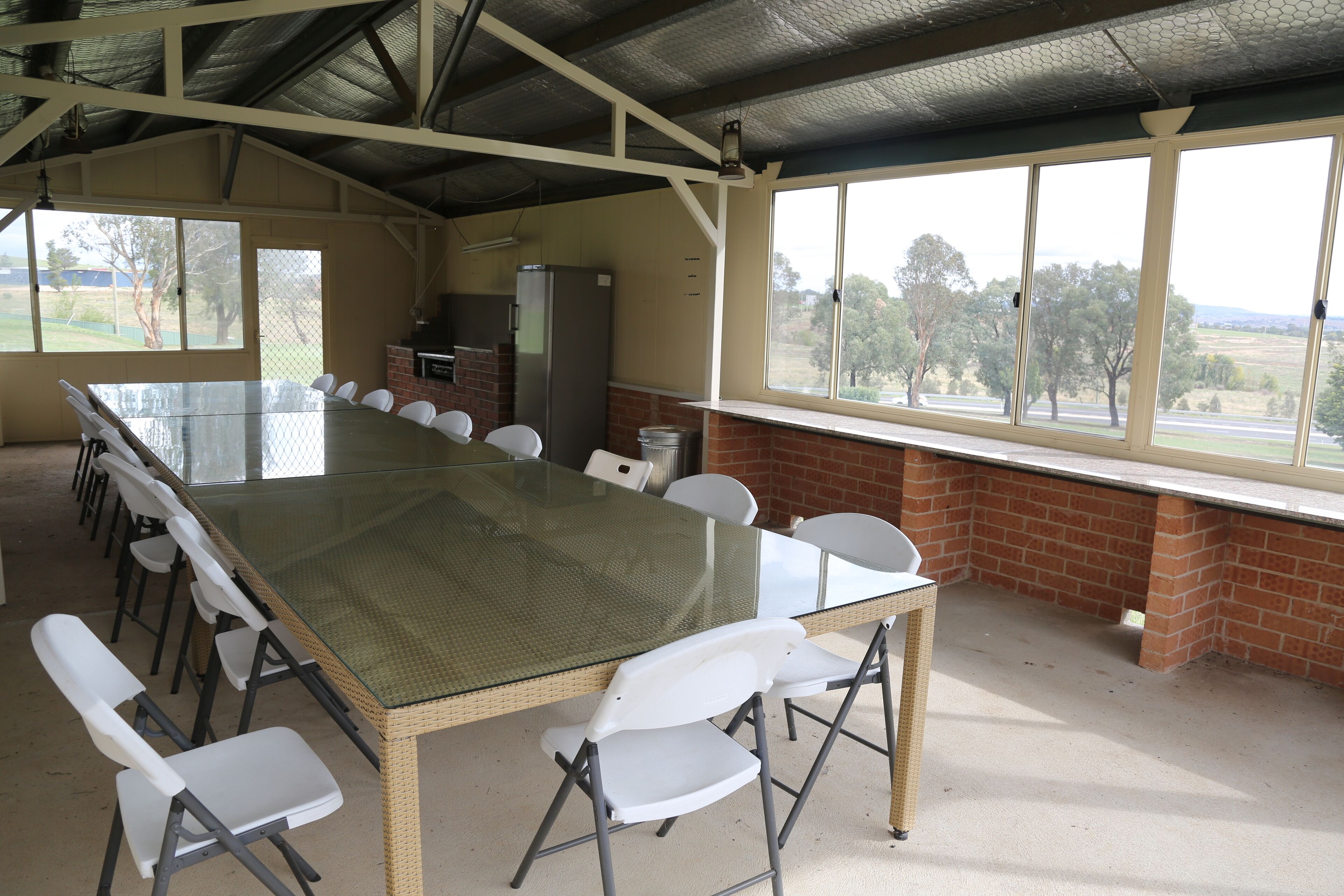 A conference room with a glass table, white chairs, a brick wall, and large windows overlooking a landscape.