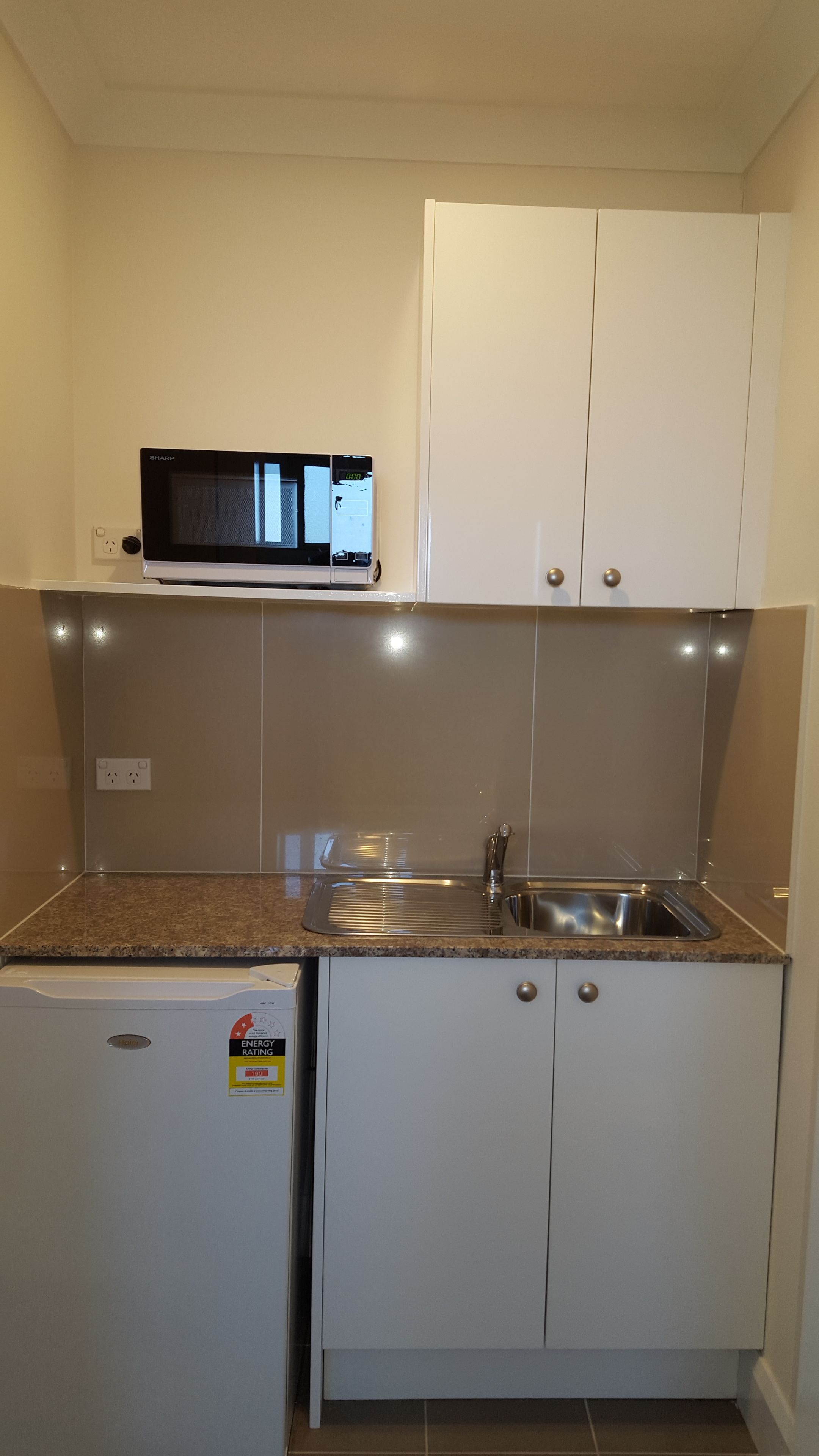 Una cocina compacta con microondas, un lavamanos y armarios.