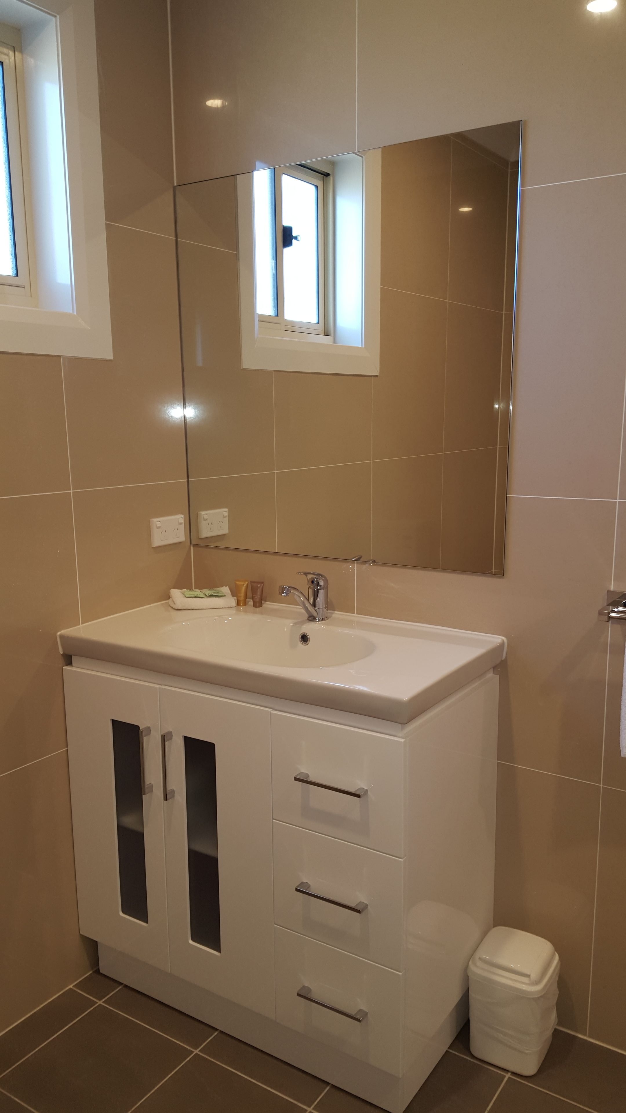 Un baño con tocador blanco, espejo y ventanal pequeño.