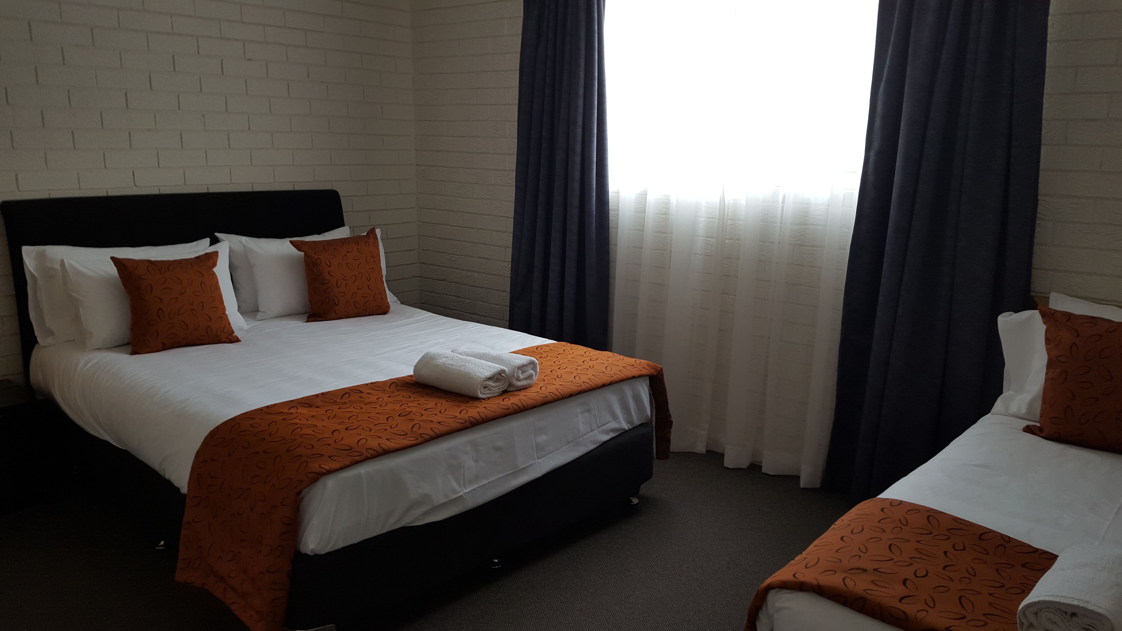 Habitación de hotel con cama doble, dos camas individuales, pared de ladrillo y ventana con cortinas.