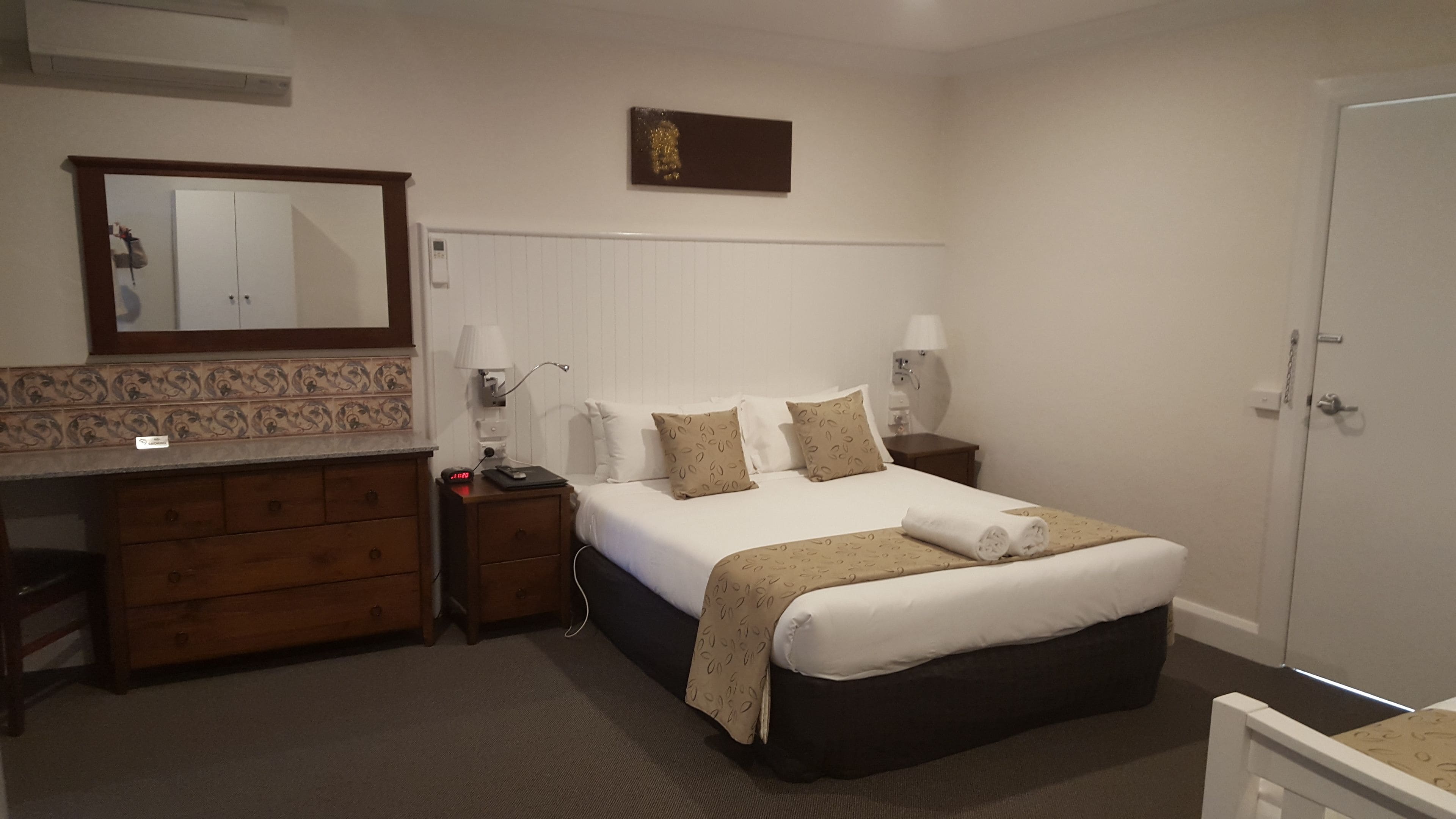 A hotel room with a bed, bedside tables, a dresser, a mirror, and a door.