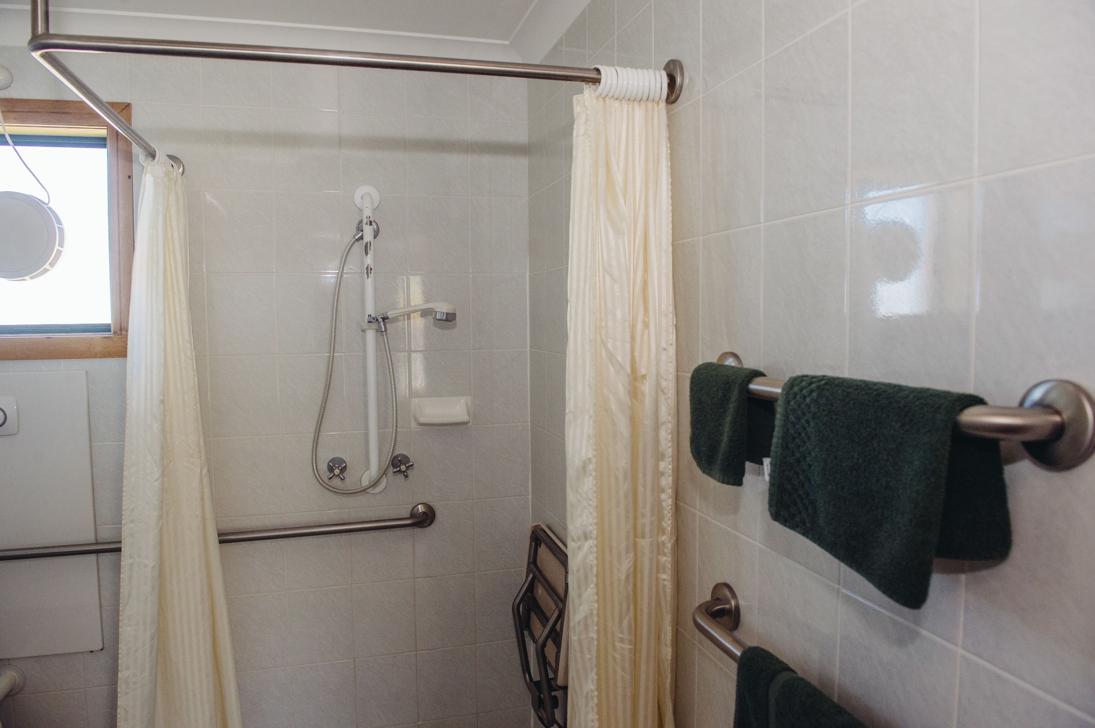 A shower area with a glass door, a towel rack with two towels, and a handrail.